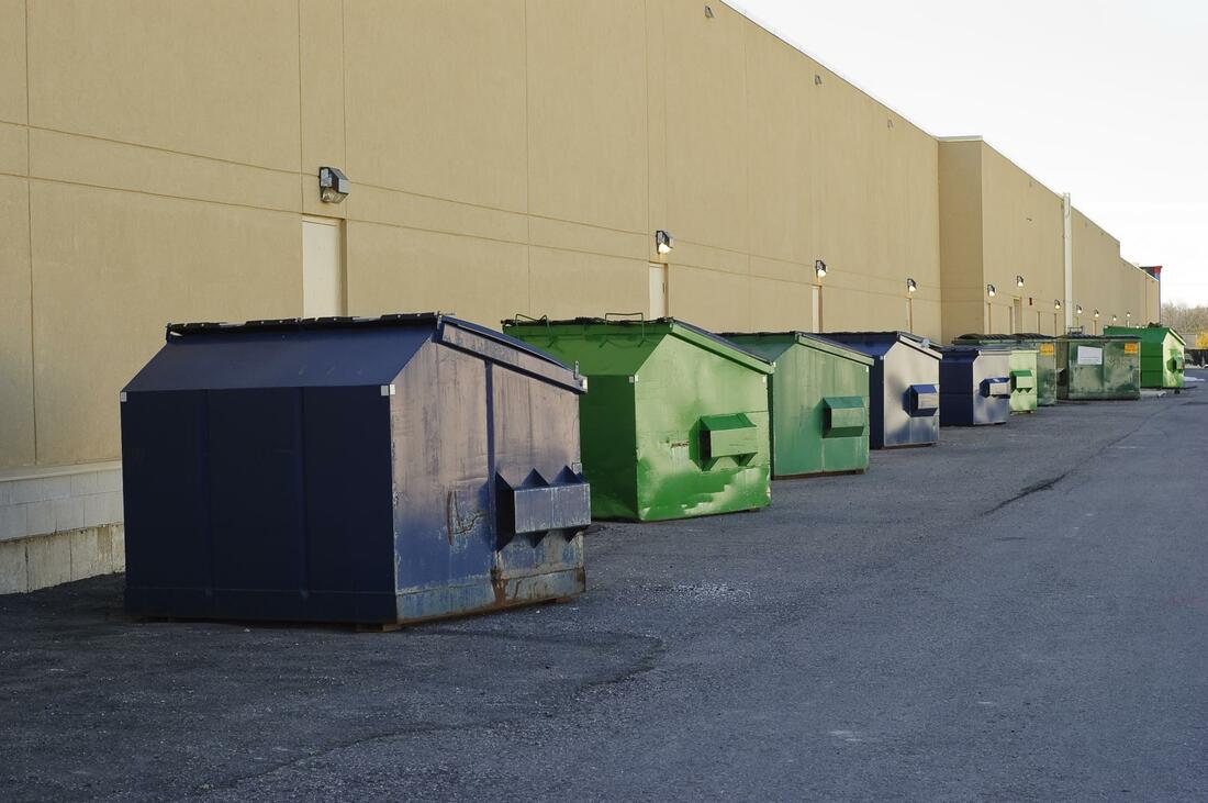 A bunch of commercial dumpsters in a line outside of a warehouse